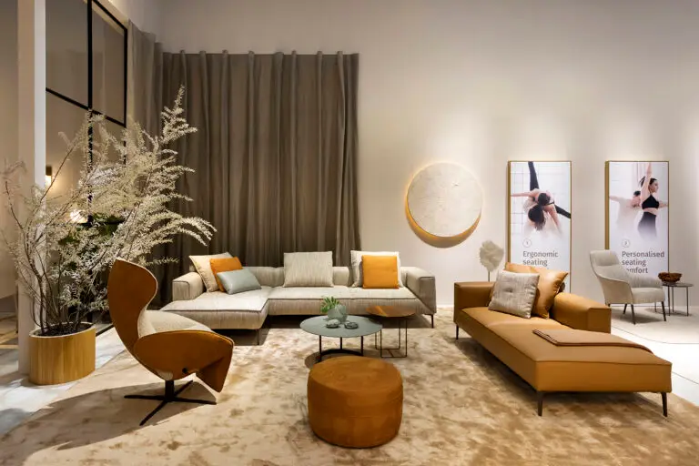 Gezellige lounge met groene en beige banken, oranje poef en kunst aan de muur